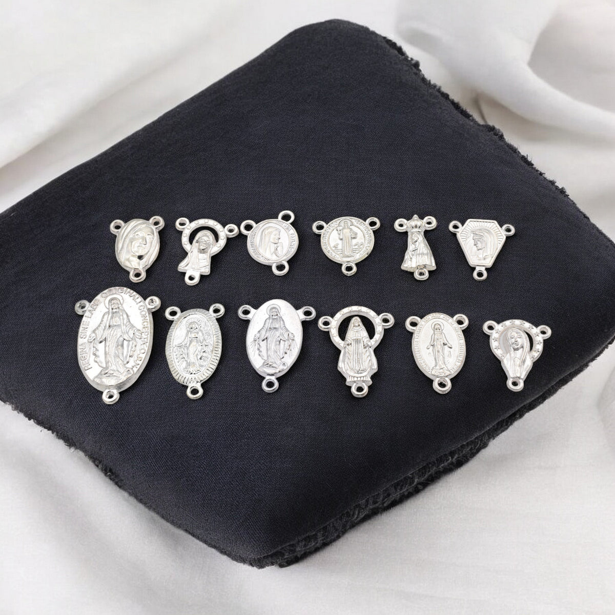 Silver religious medallions on black fabric background.