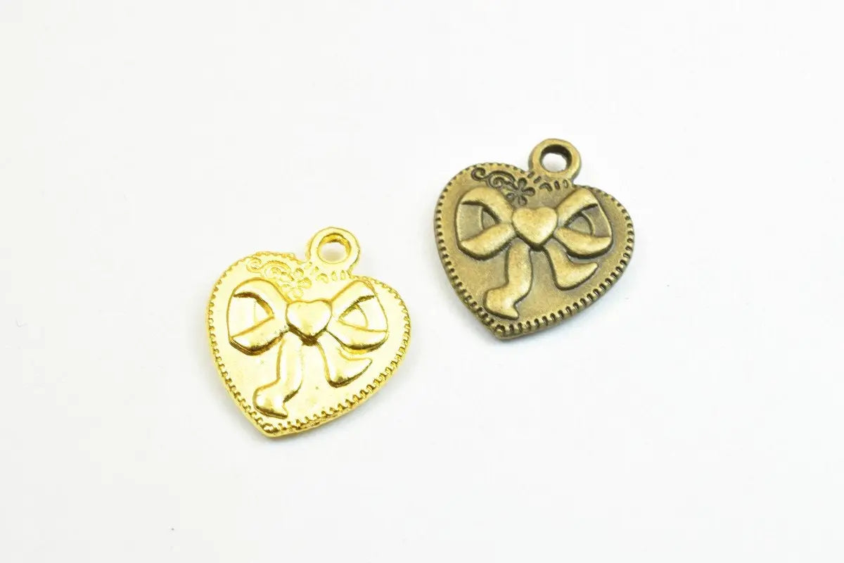 Heart-shaped metal charms with bow design in gold and bronze tones.