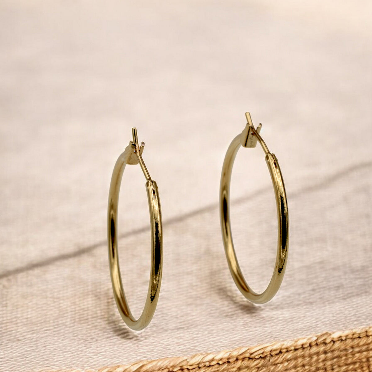 Close-up view of chunky gold hoop earrings with a polished finish, placed on a fabric background for an elegant look.