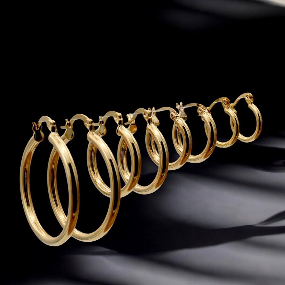 Set of gold hoop earrings in multiple sizes displayed on a black background, emphasizing their shiny, reflective surface and classic design.