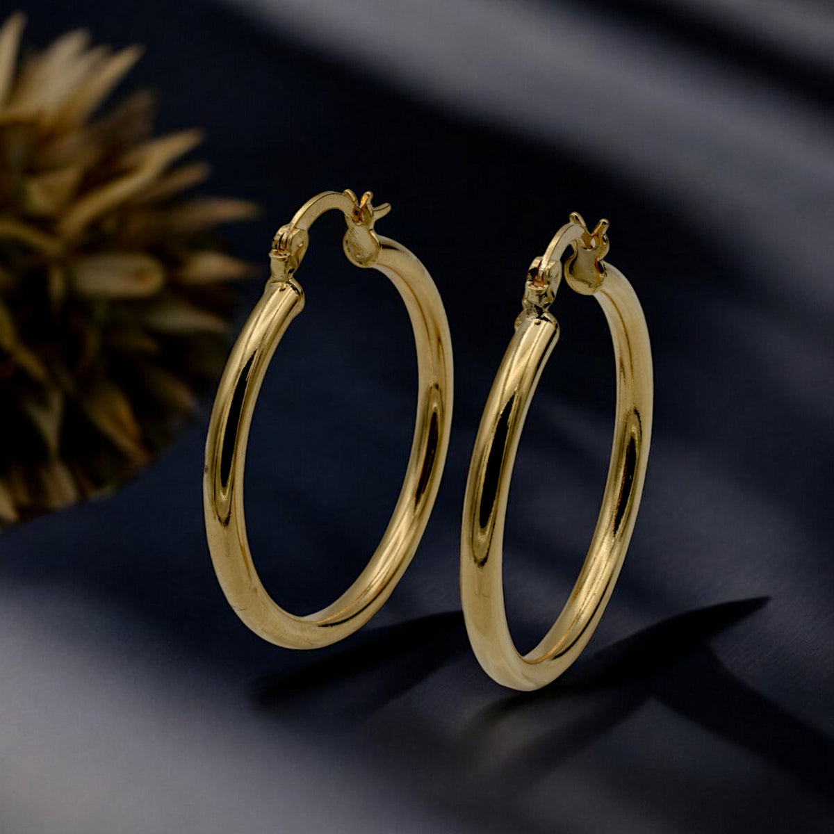 Set of gold hoop earrings in multiple sizes displayed on a black background, emphasizing their shiny, reflective surface and classic design.