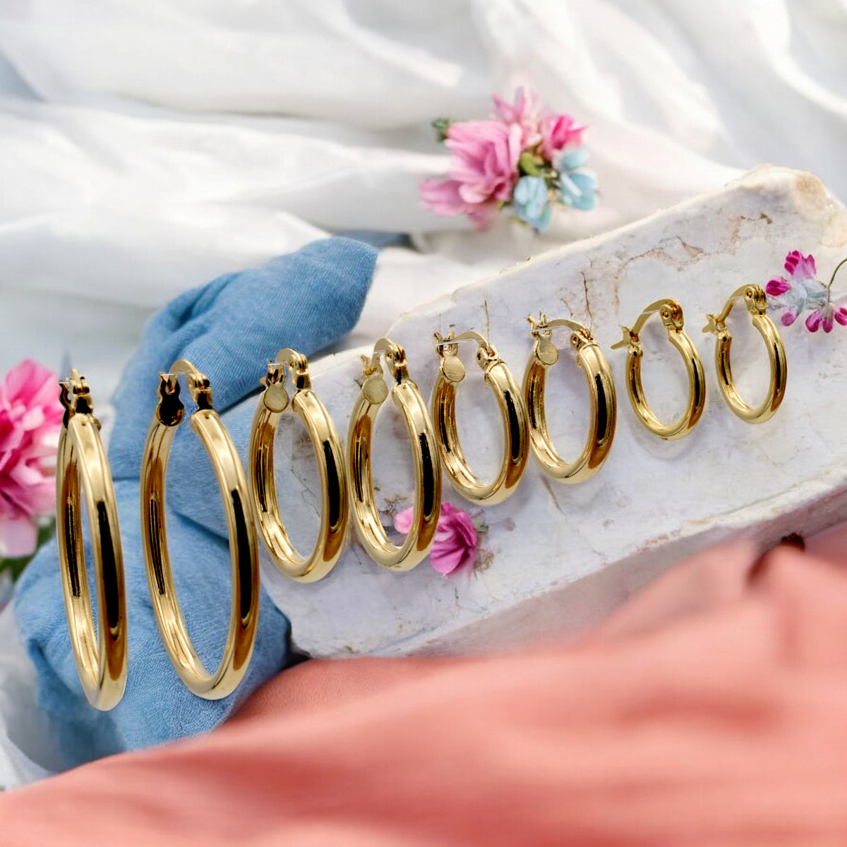 Set of gold hoop earrings in multiple sizes displayed on a black background, emphasizing their shiny, reflective surface and classic design.