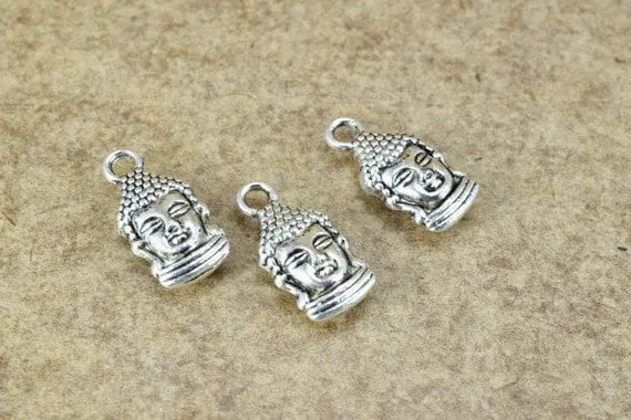 Silver Buddha head charms on a textured beige background.