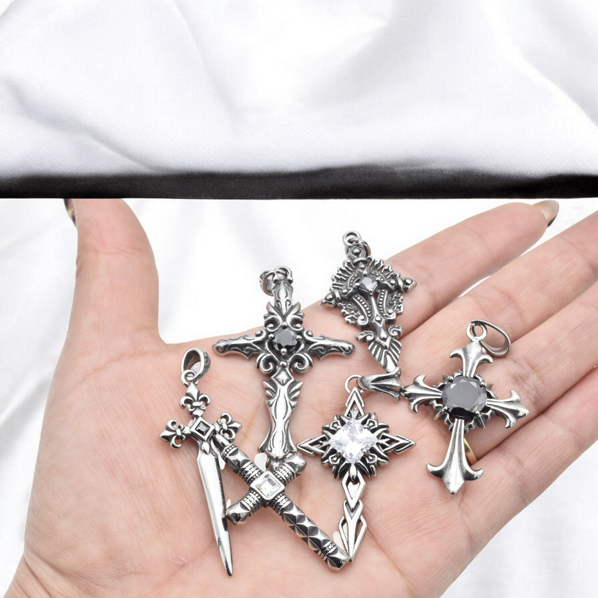 Hand holding five silver cross sword pendants with black gemstones.