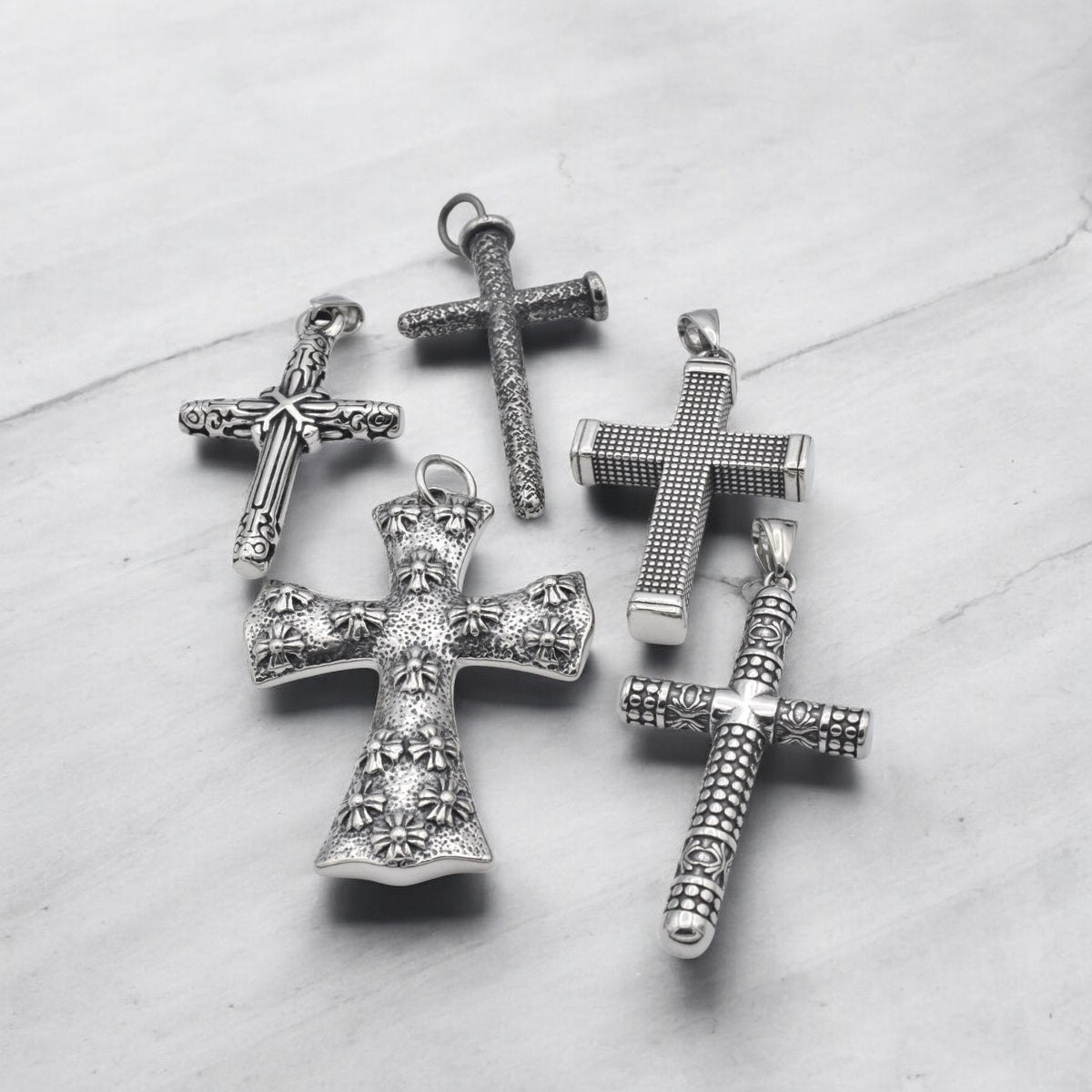 Vintage silver cross pendants with intricate designs on marble background.
