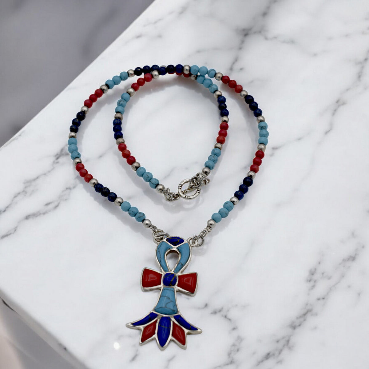 Colorful beaded necklace with red, blue, and silver beads featuring a decorative pendant on marble surface.