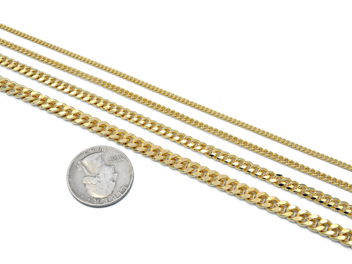 A sun-drenched lifestyle shot of gold-tone chains reflecting natural sunlight on a wooden deck by the water, emphasizing the premium 14K gold look and shine.