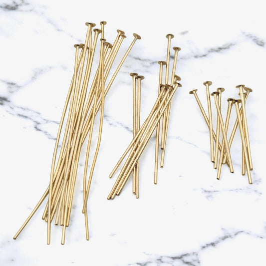A group of gold-finished flat head pins in three different lengths (20mm, 30mm, and 50mm) fanned out on a white surface. The image highlights the smooth, polished gold finish and the consistent flat-head base of each pin.