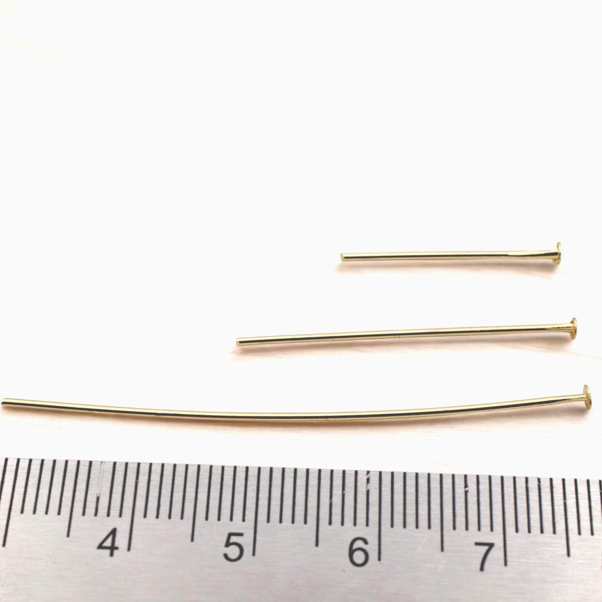 A close-up of a model wearing finished gold dangle earrings, showing how the gold head pins provide a clean, elegant finish to high-end handmade jewelry.