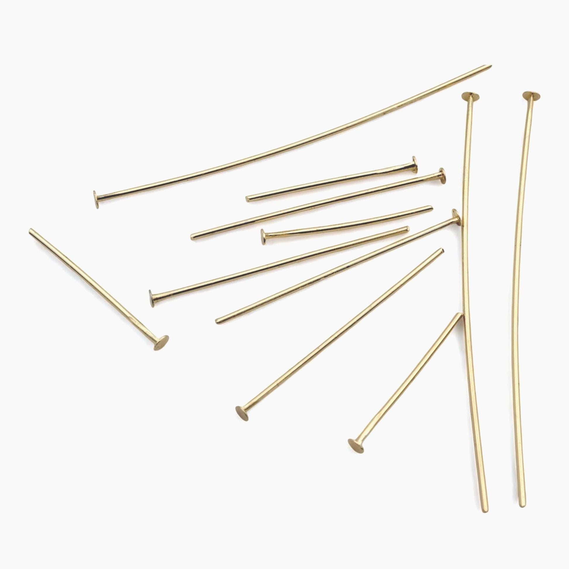 A large pile of 100 gold-finished head pins scattered on a clean background, representing the bulk wholesale pack available for professional crafters and small businesses.