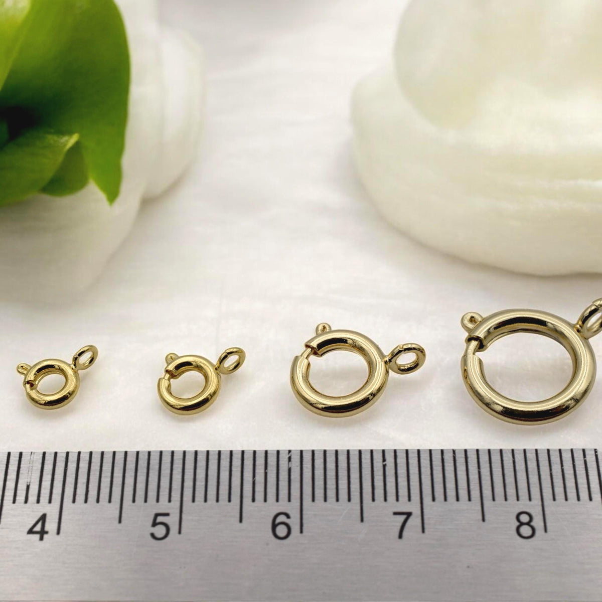Gold-filled round clasp in use on a handmade bracelet, photographed on a textured background with dried flowers.