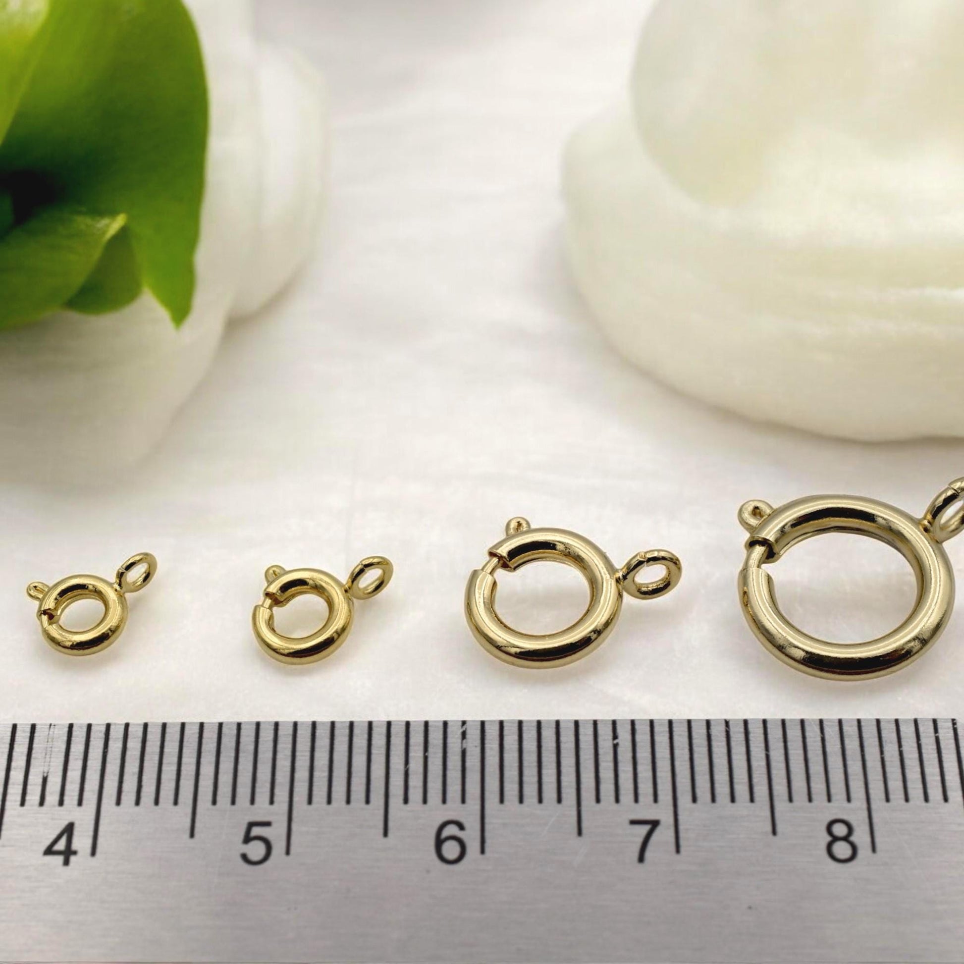 Gold-filled round clasp in use on a handmade bracelet, photographed on a textured background with dried flowers.