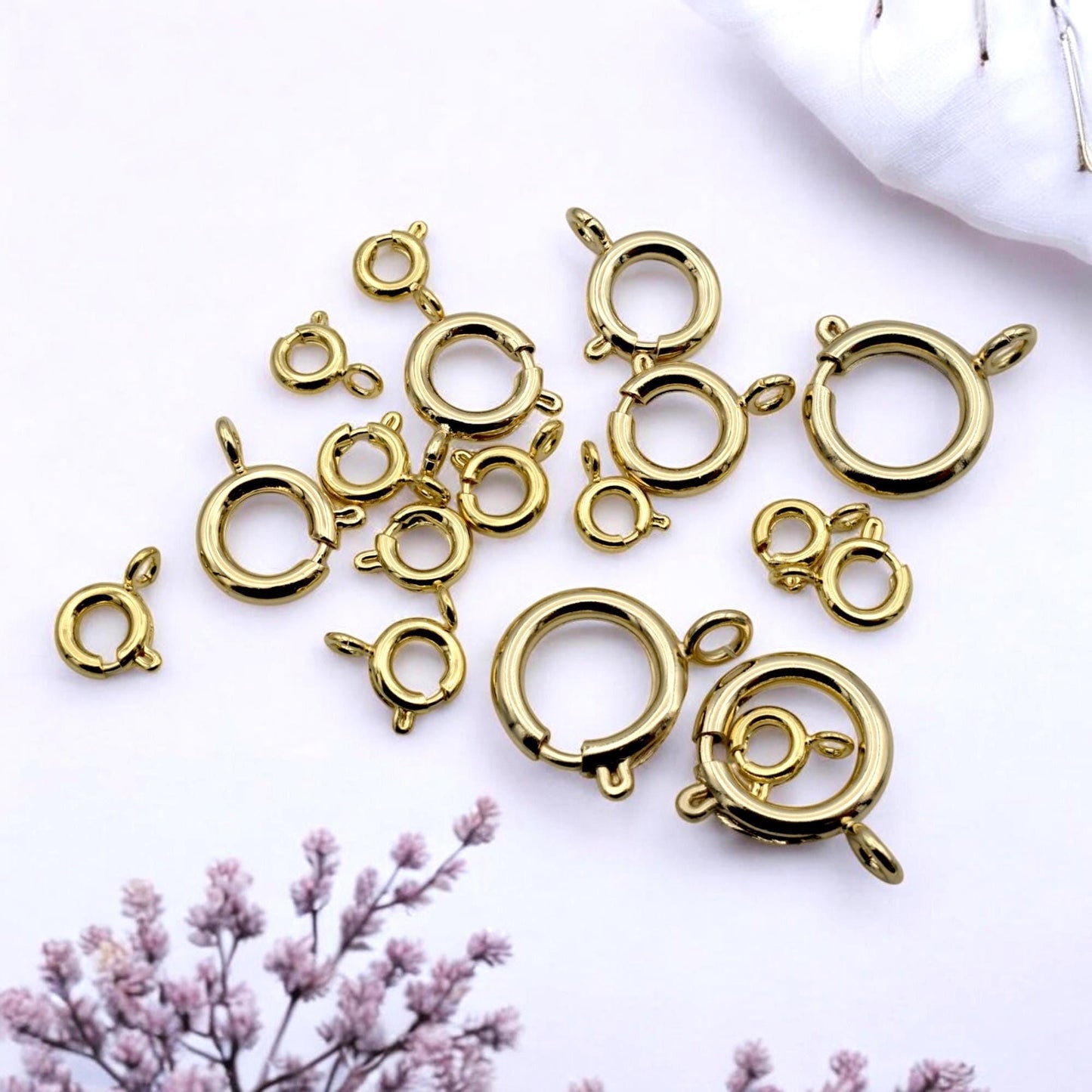 Assorted gold-filled spring clasps in various sizes arranged on a neutral fabric surface for jewelry design.