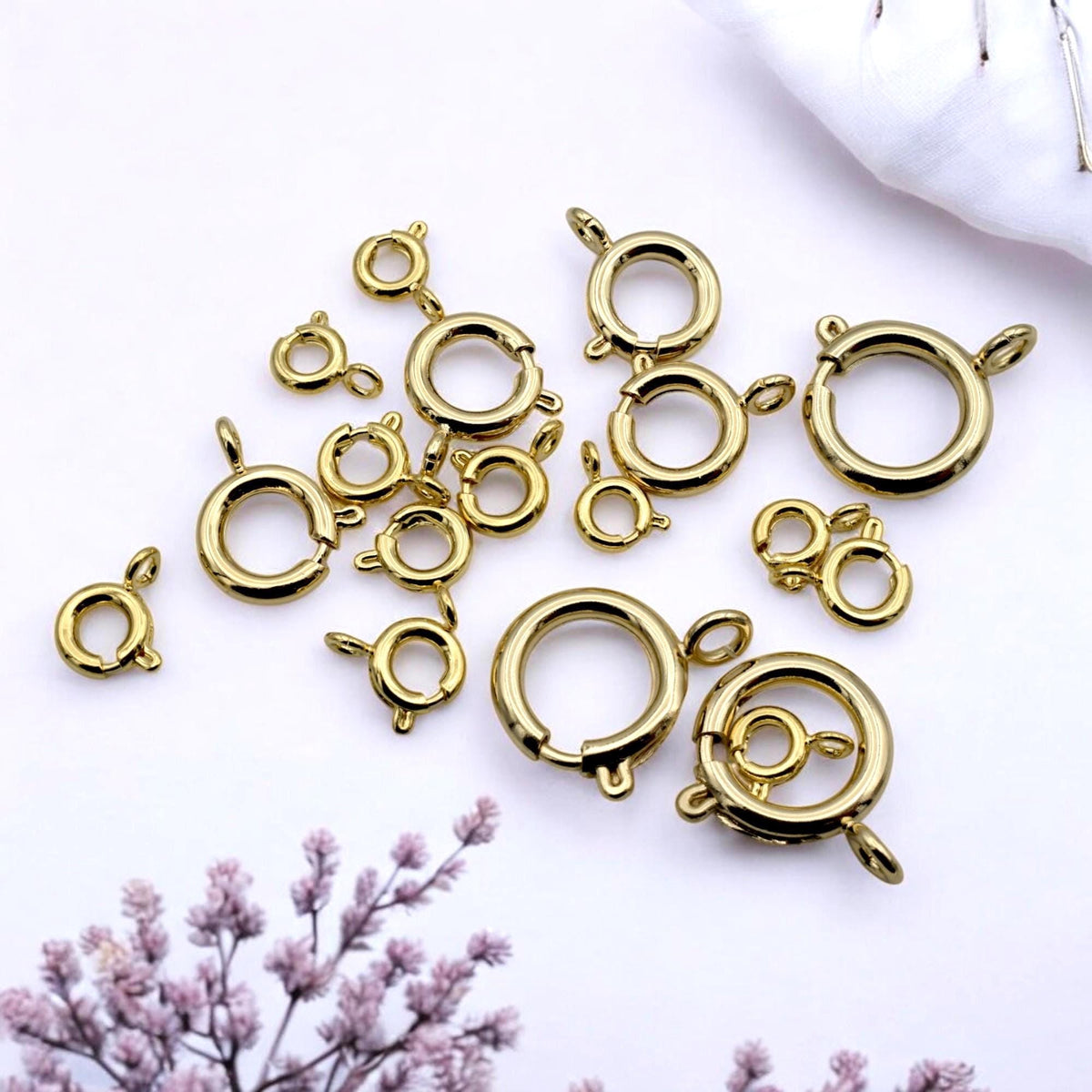 Assorted gold-filled spring clasps in various sizes arranged on a neutral fabric surface for jewelry design.