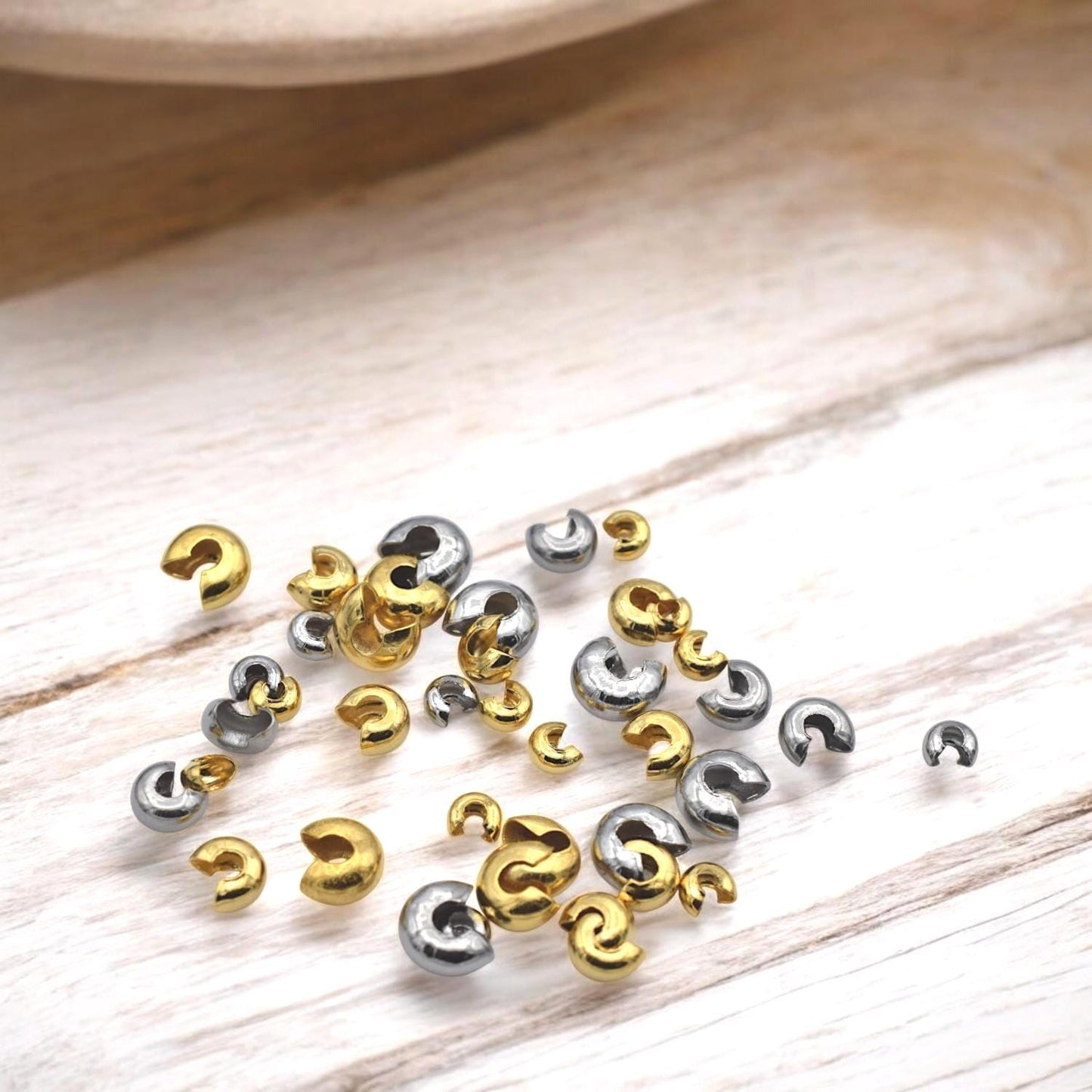 Gold crimp covers placed beside stretch cord and beading wire, ideal for professional bracelet and necklace endings