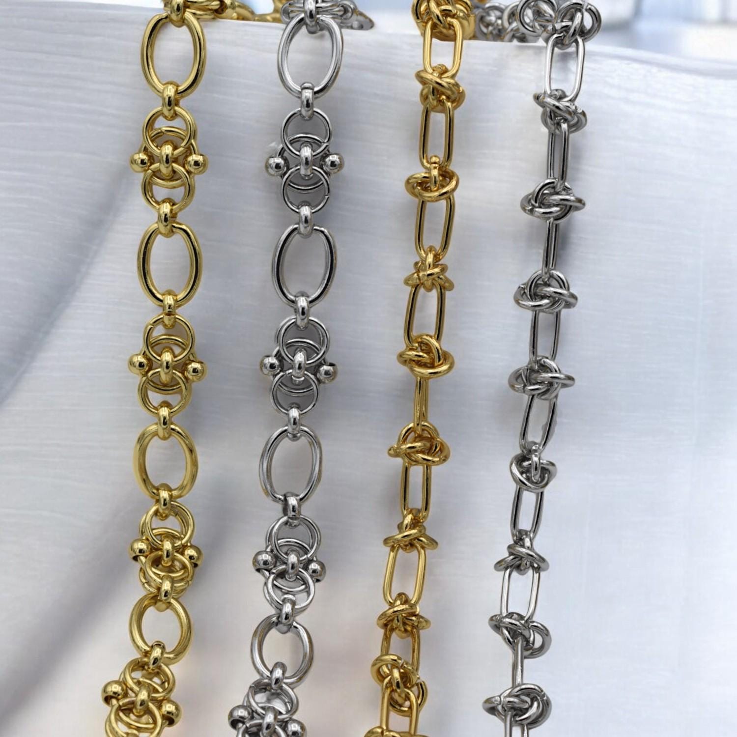 Gold knot-style jewelry chain with oval links and decorative loops, laid flat on a white textured surface.