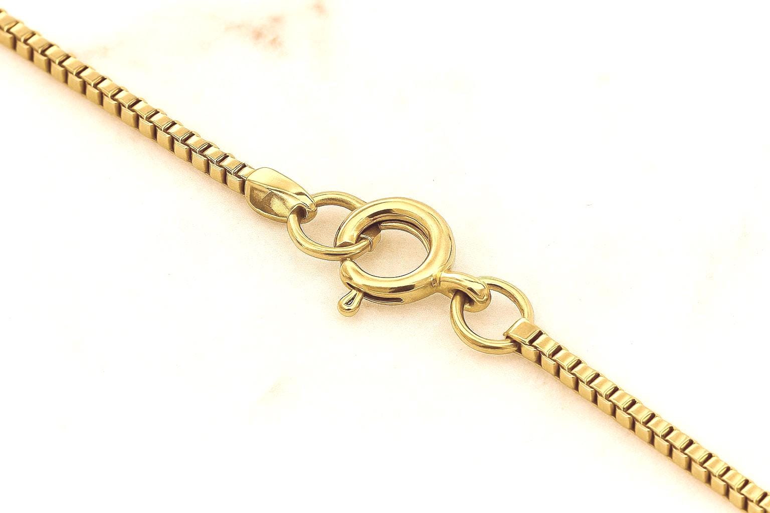 Gold-filled circular clasp attached to a delicate chain, highlighting its secure closure and polished finish.