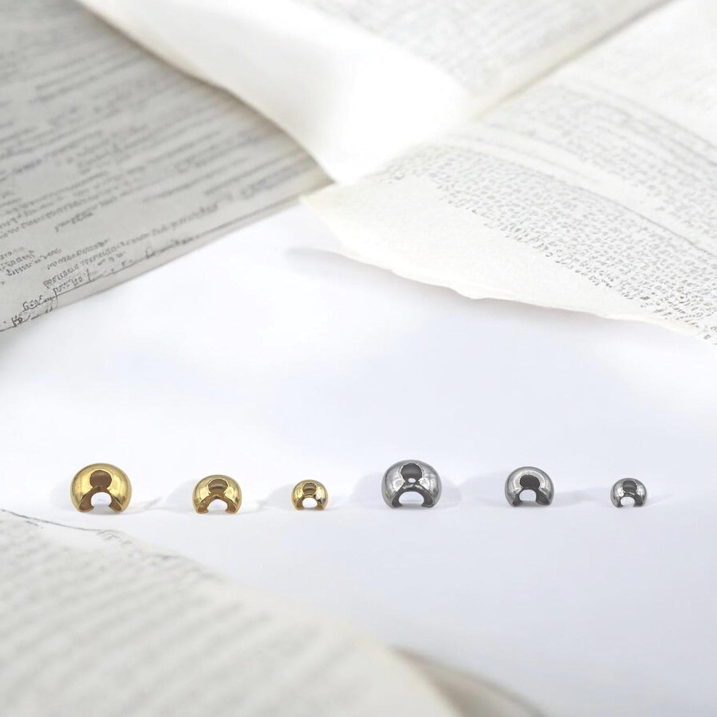 Close-up of gold stainless steel dome crimp covers in multiple sizes, displayed on a white background for jewelry making.