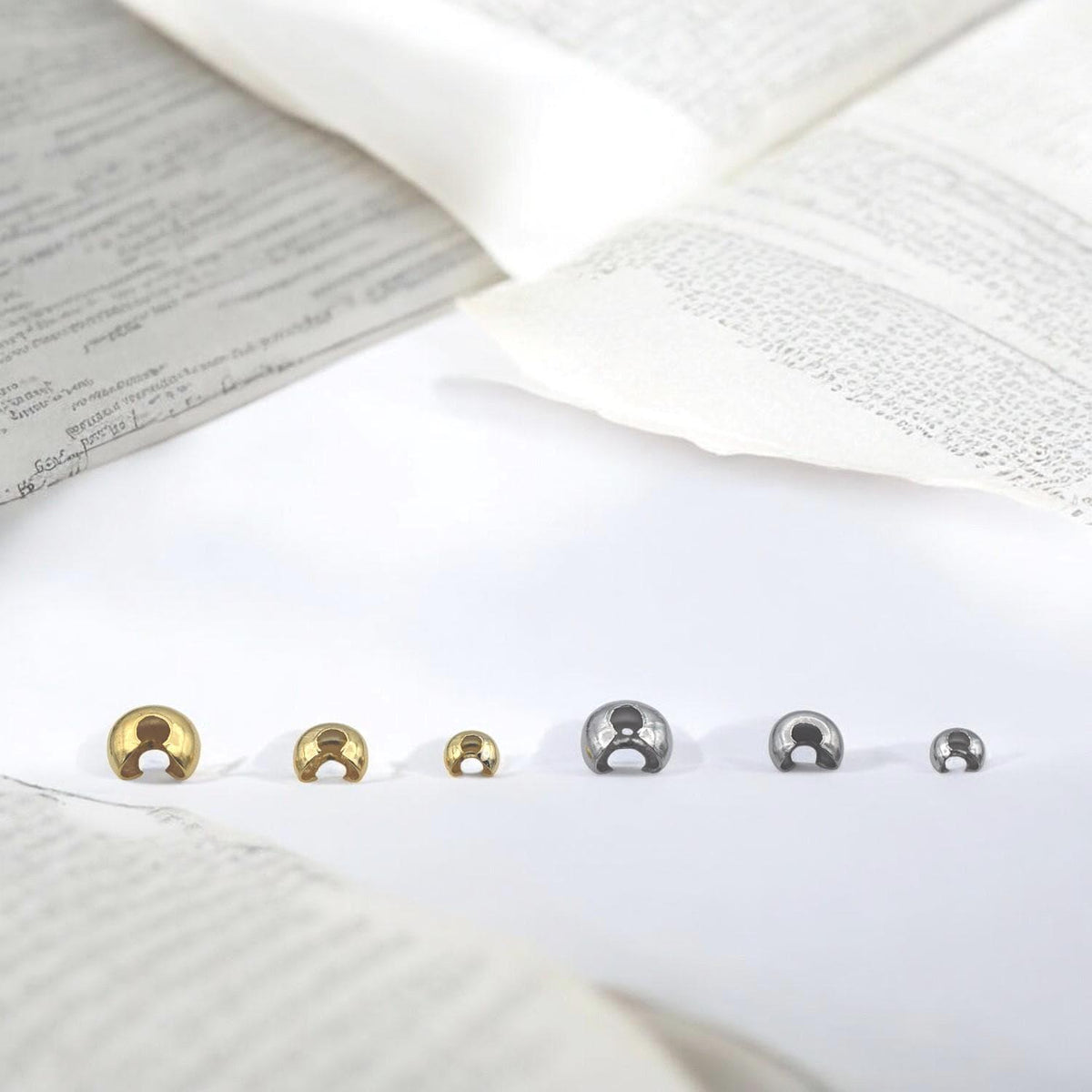 Close-up of gold stainless steel dome crimp covers in multiple sizes, displayed on a white background for jewelry making.