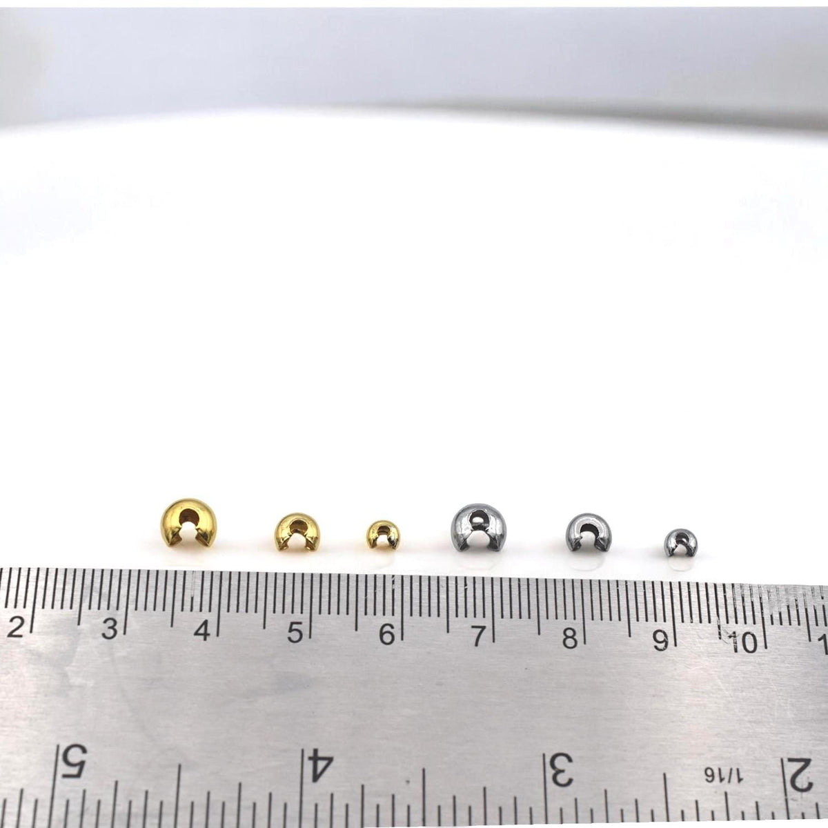 Assorted gold knot covers arranged in a row, showing size variations for hiding crimps and knots in bracelets and necklaces.