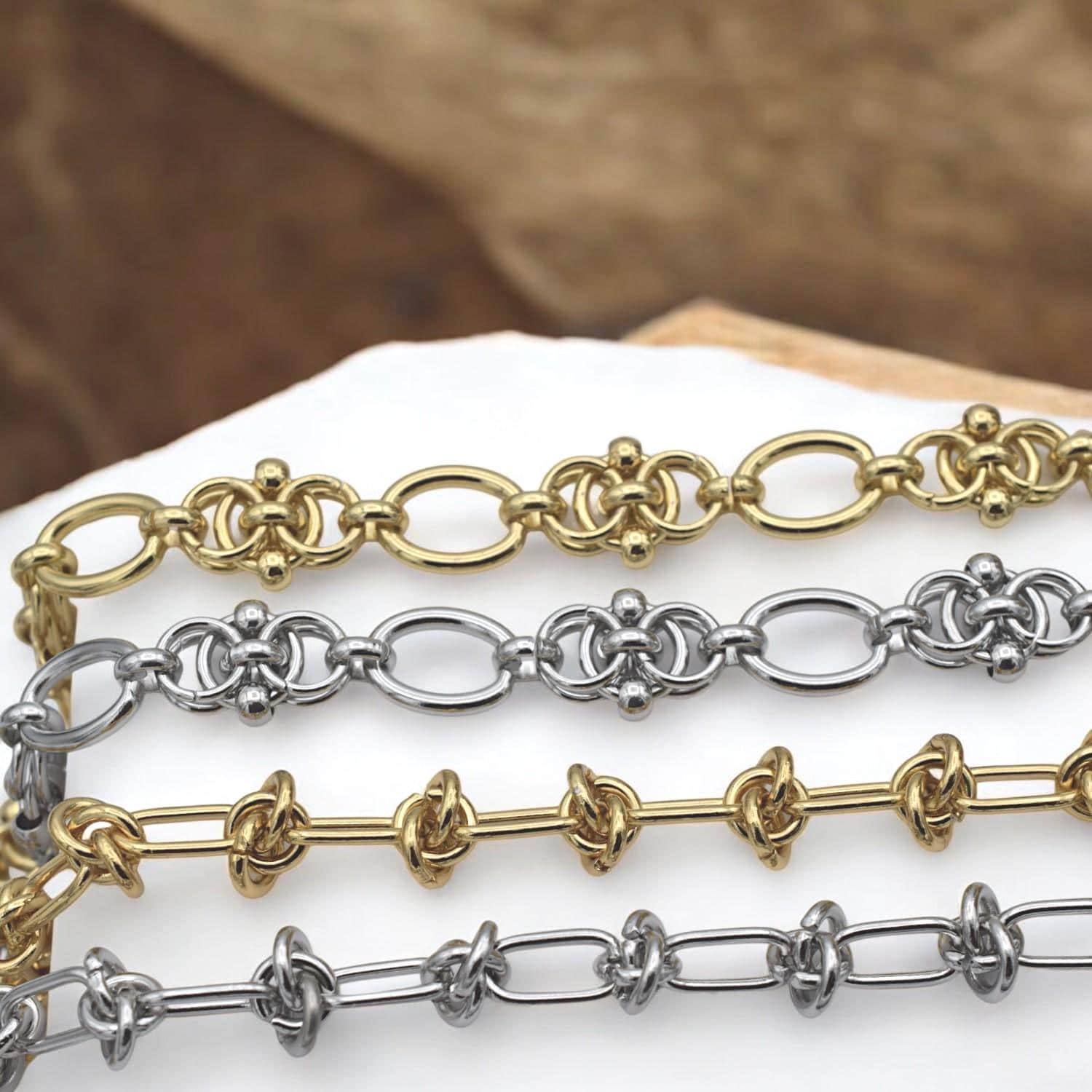 Side-by-side comparison of gold and silver knot chains with alternating link styles, displayed on neutral fabric.