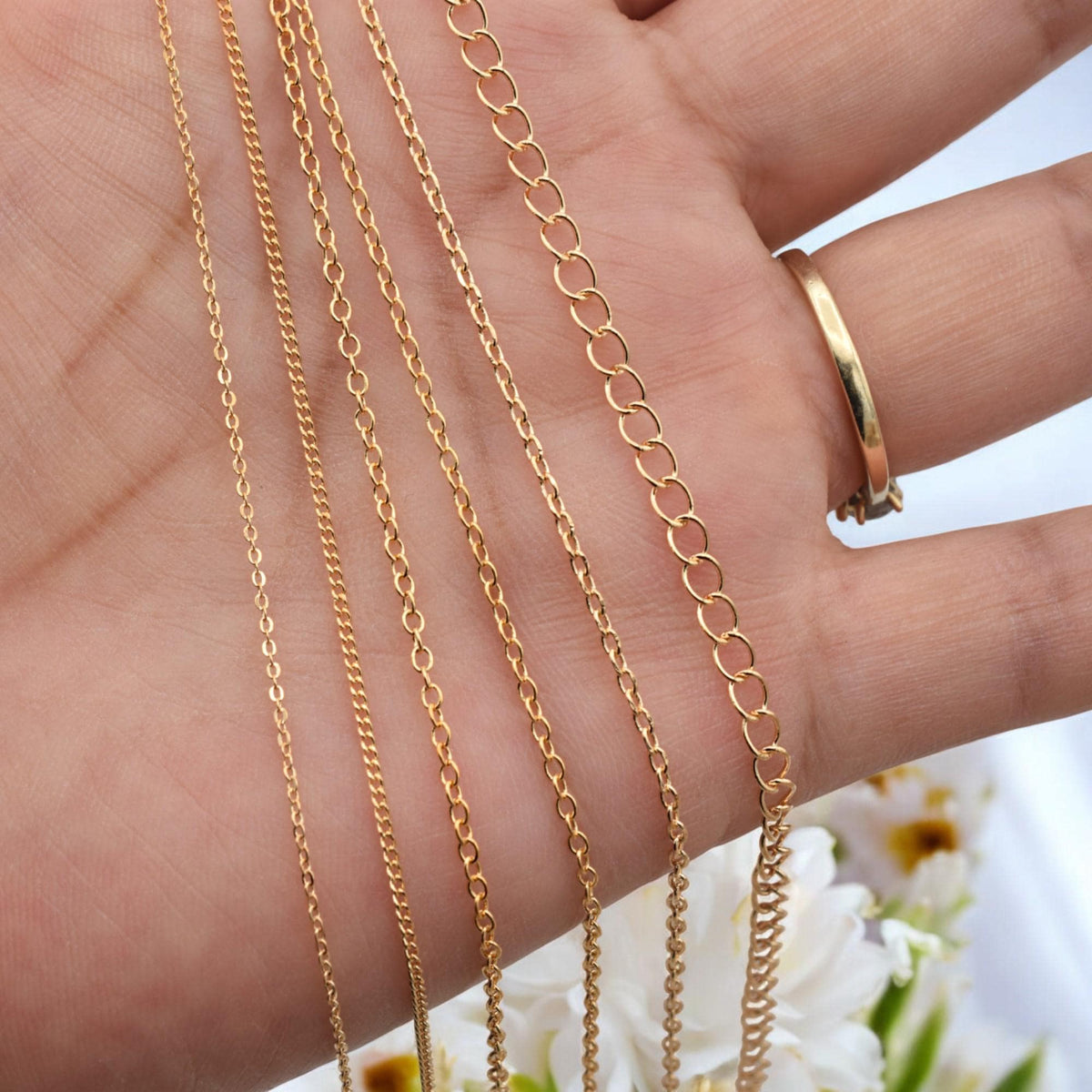 Detailed view of dainty and bold gold cable chains laid across skin for scale reference