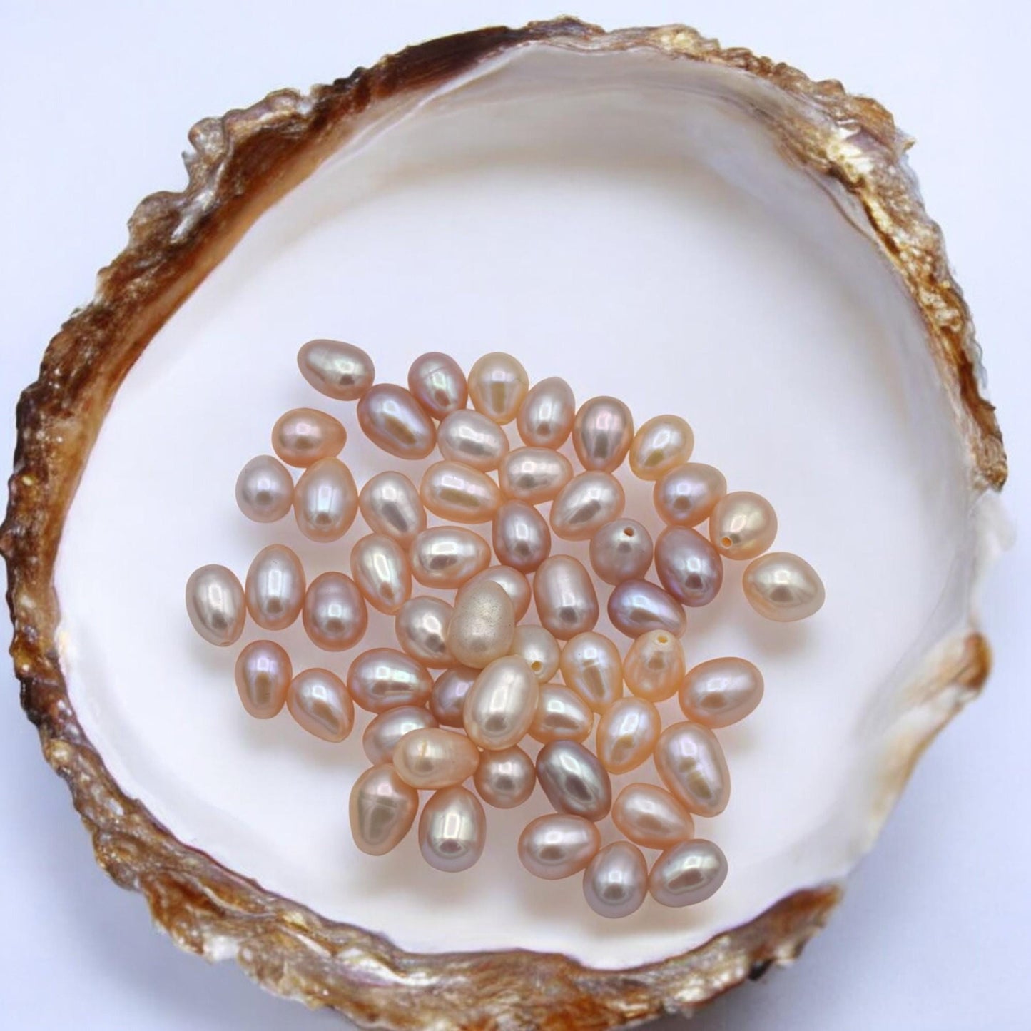 Assorted freshwater pearls in white, cream, black, and blush pink tones.
Perlas de agua dulce surtidas en tonos blanco, crema, negro y rosa suave.