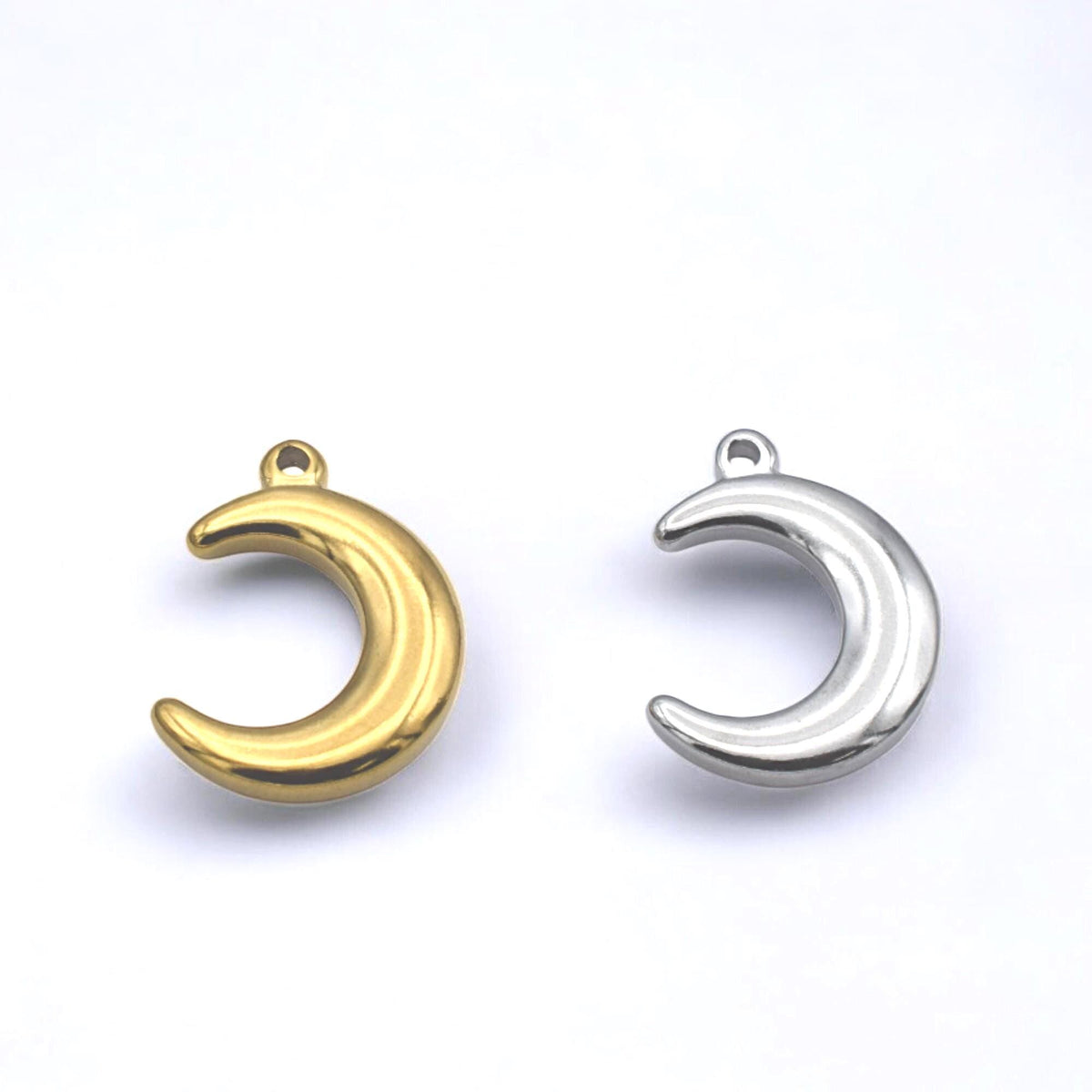 Close‑up of stainless steel crescent moon charm showing smooth, puffy shape.
Primer plano del colgante de luna creciente en acero inoxidable con forma abultada y suave.