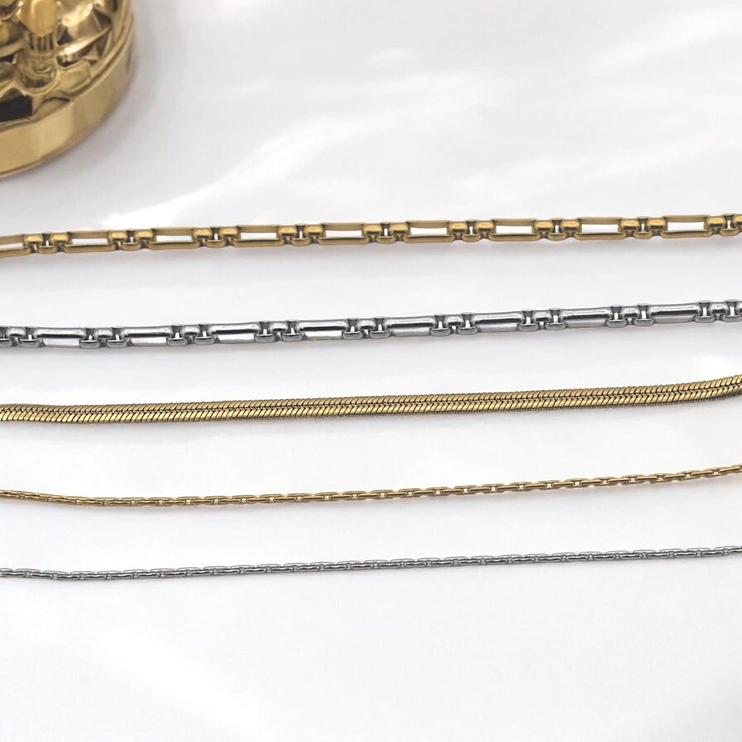 Layering necklace styled with box and snake chains in gold and silver tones.