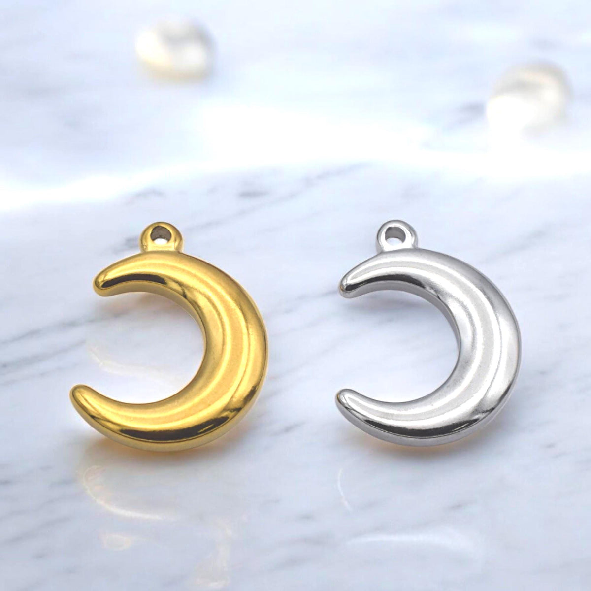 Pack of three stainless steel moon charms arranged neatly together.
Paquete de tres charms de luna en acero inoxidable colocados de forma ordenada.