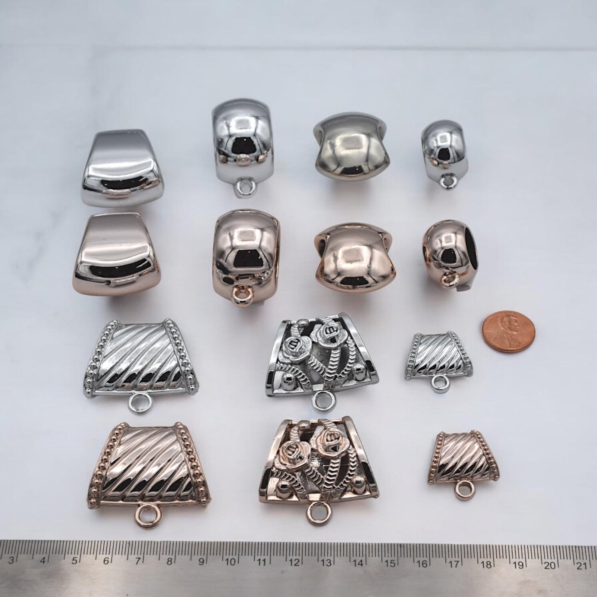 Cuentas con asa en plata, oro y oro rosa sobre fondo texturizado.
Silver, gold, and rose gold loop bail beads displayed on textured background.
