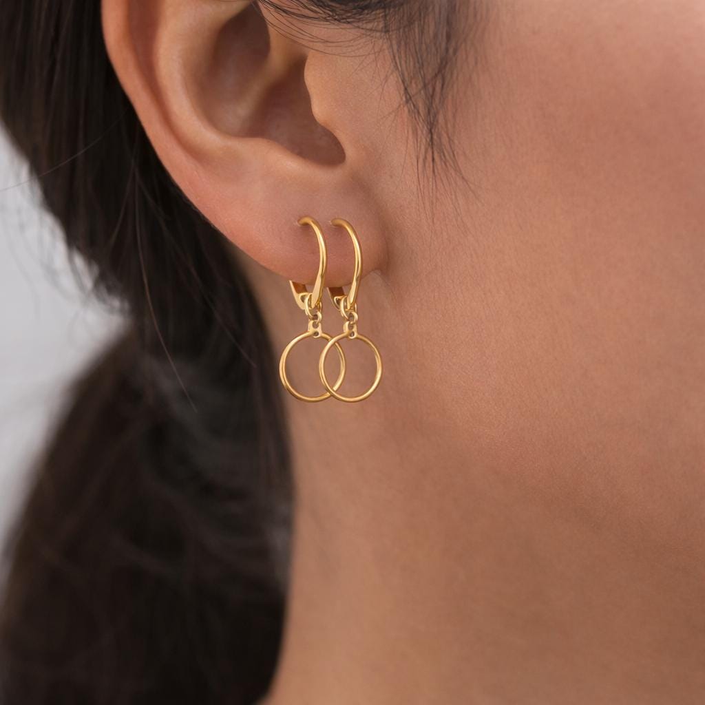 Ganchos y aros dorados exhibidos con flores suaves de cerezo rosado.
Gold earring hooks and hoops displayed with soft pink cherry blossom flowers.