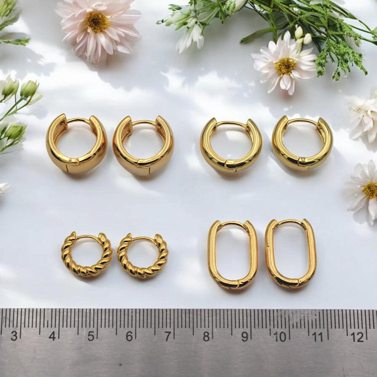 A group of various gold hoop earring findings arranged on a white surface to show the different shapes and sizes available.
