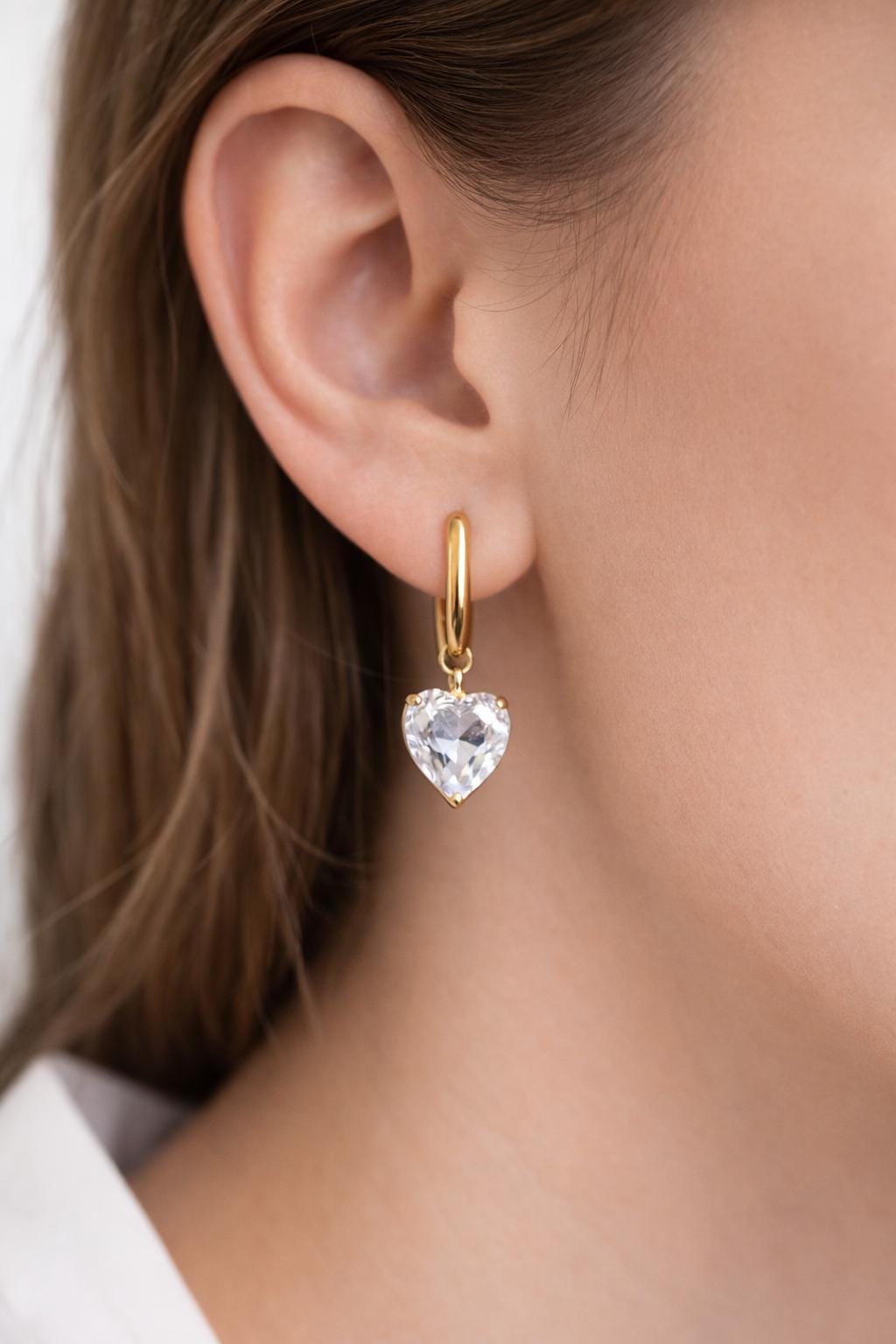 A close-up side view of a model wearing the polished oval gold hoops, showing how they sit comfortably on the earlobe.