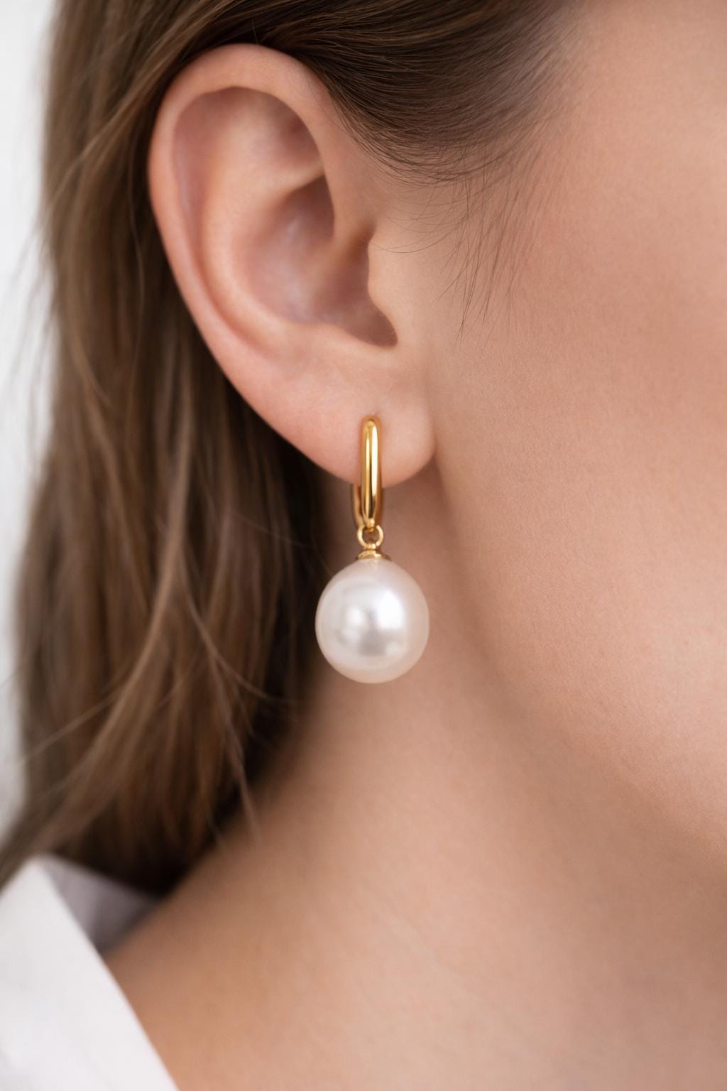 A person wearing the chunky 18k gold-filled huggie hoops with a pearl charm attached, demonstrating how to customize the findings.