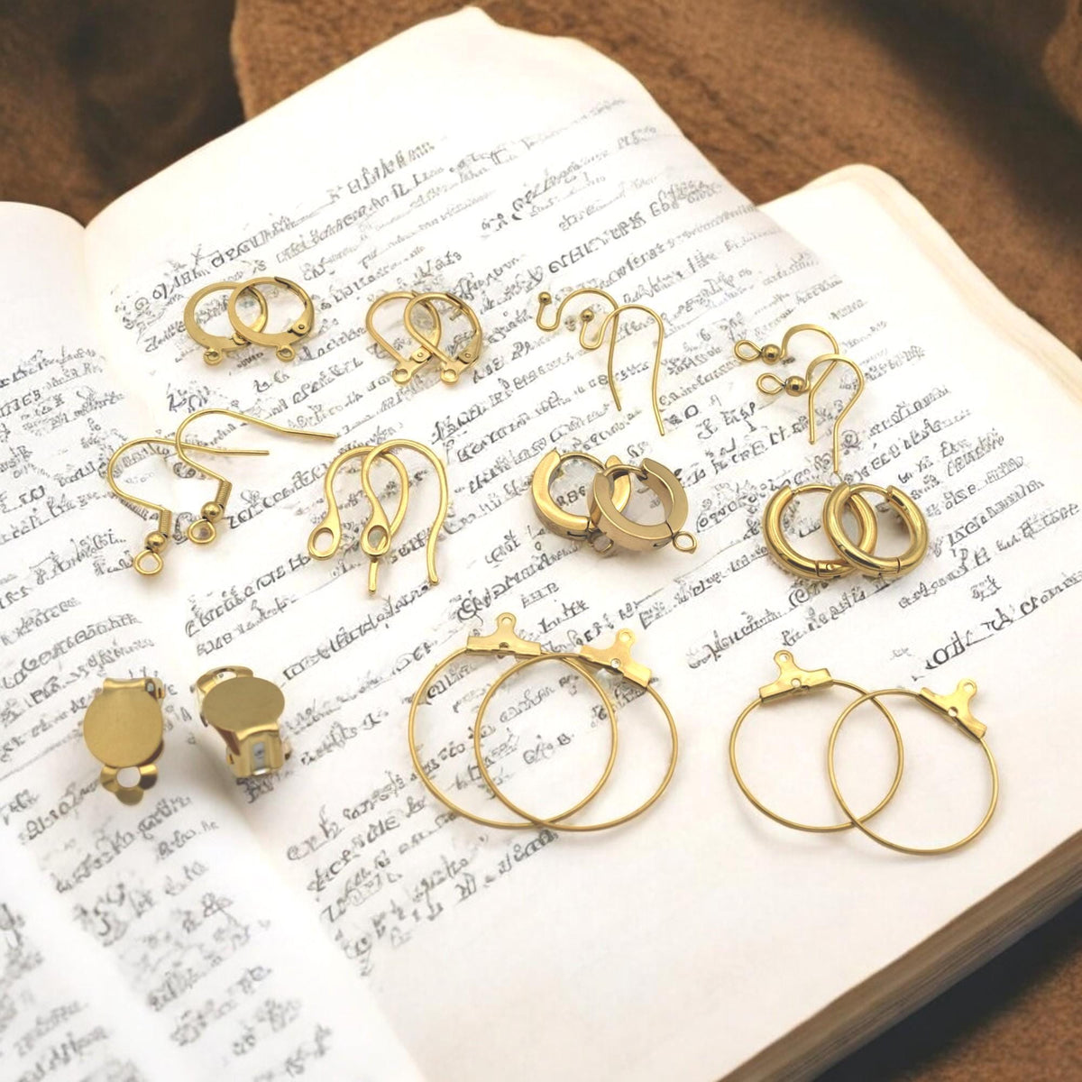 Flat lay de componentes dorados sobre fondo blanco brillante con reflejos.
Flat lay of gold earring components on glossy white background with reflections.