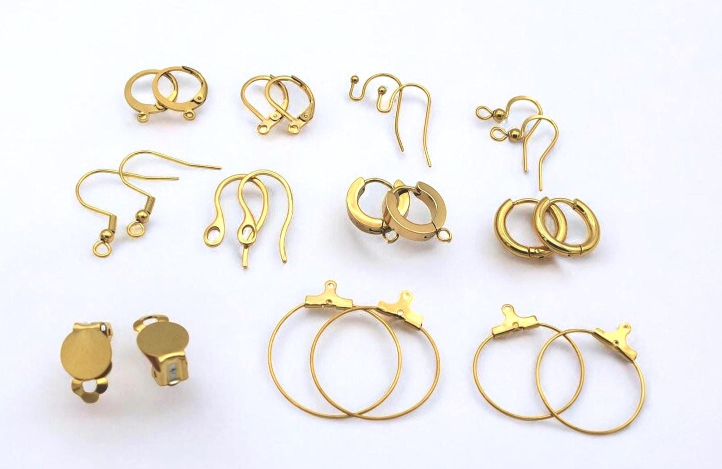 Ganchos dorados tipo fishhook con detalle de bola y espiral junto a flores suaves.
Gold fishhook ear wires with ball and coil detail shown with soft floral decor.
