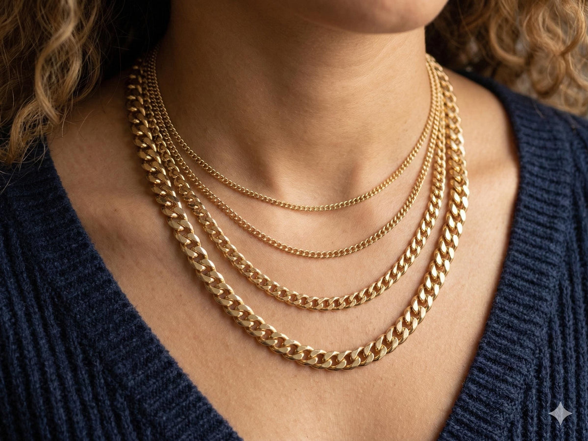 Lifestyle photo of a woman wearing four layers of gold curb chains over a navy blue sweater, showing the graduation of 2.2mm, 3.5mm, 4.5mm, and 6mm widths.
