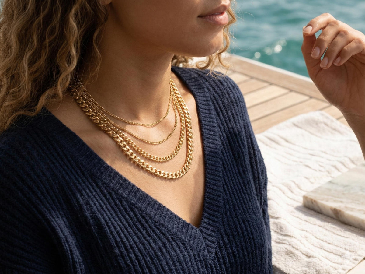 Lifestyle photo of a woman wearing four layers of gold curb chains over a navy blue sweater, showing the graduation of 2.2mm, 3.5mm, 4.5mm, and 6mm widths.