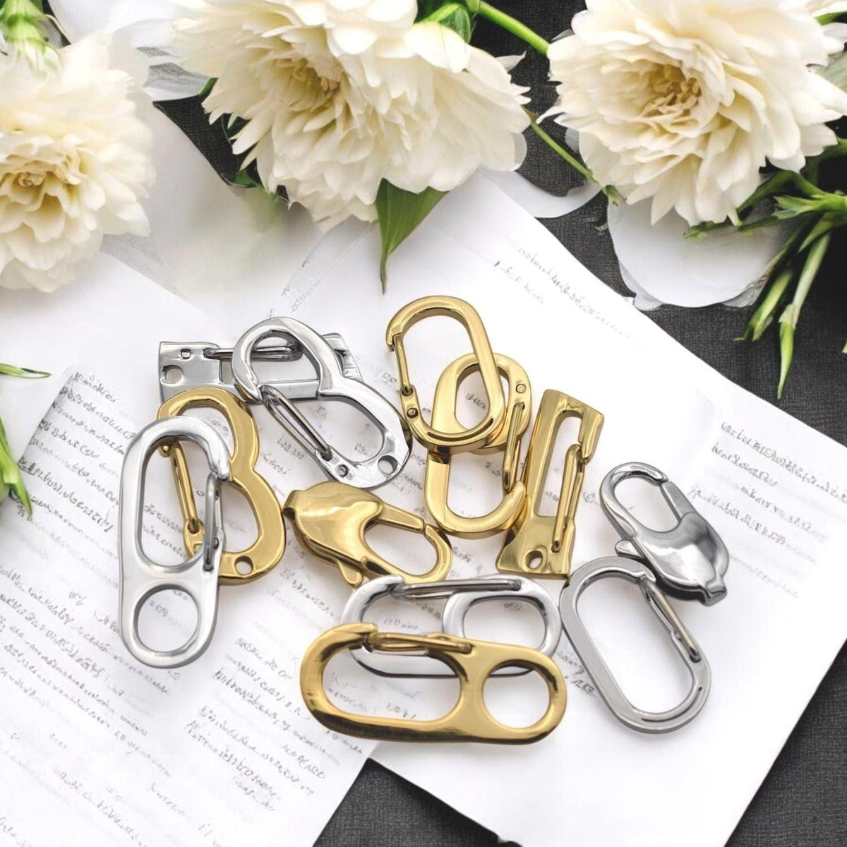 a collection of various metal keys, including a keychain, arranged on a piece of paper with white flowers in the background.
