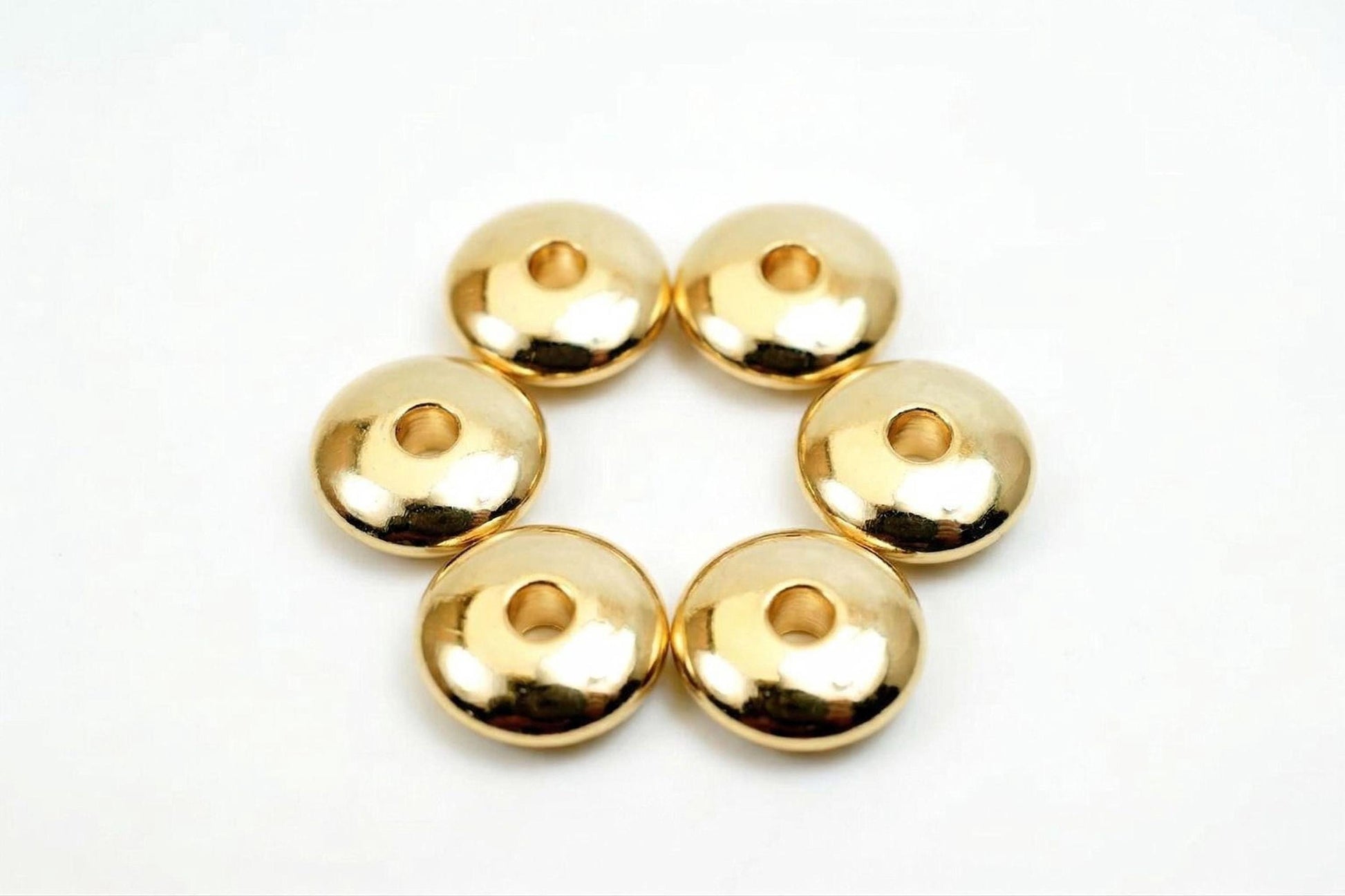 Six shiny gold-colored beads arranged in a circular pattern on a white background.