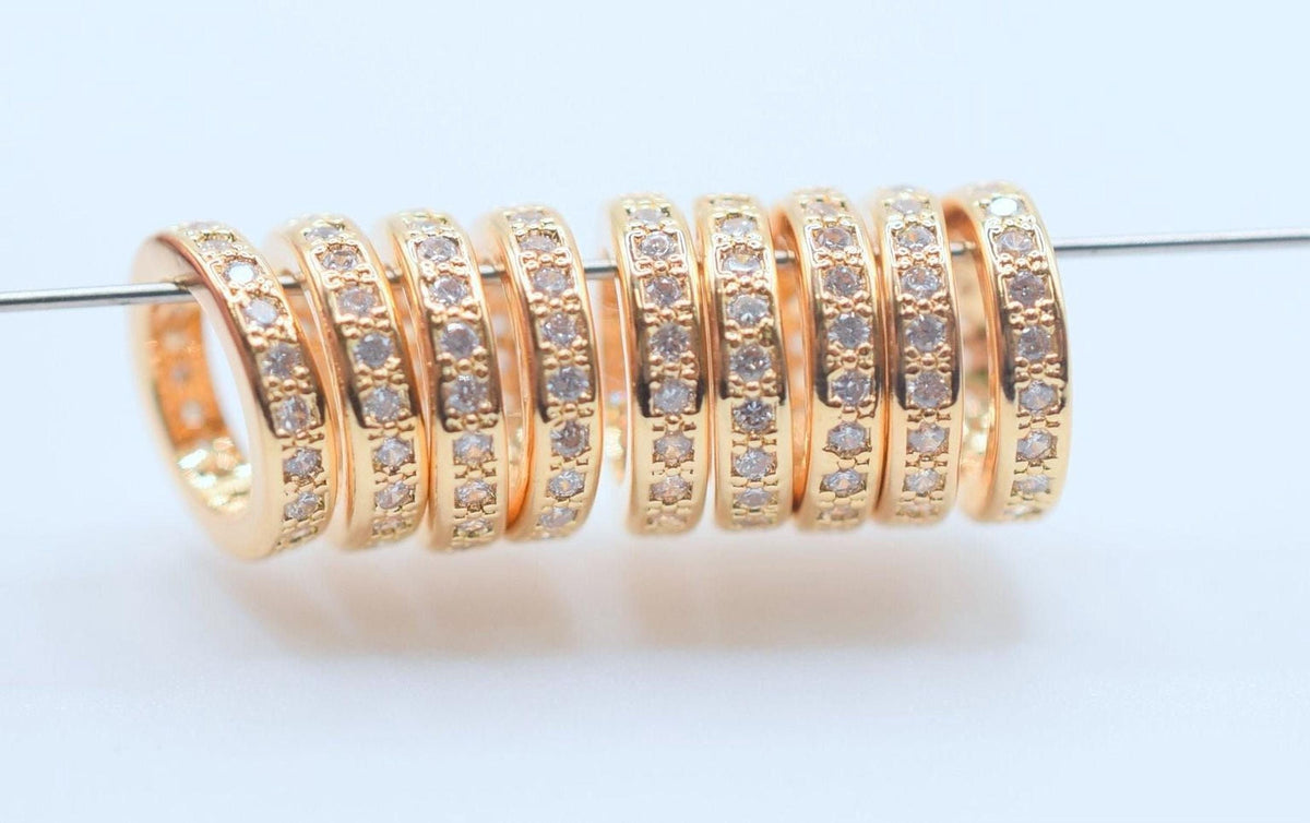 A row of gold-colored rings with small diamonds set in them, arranged on a white surface.