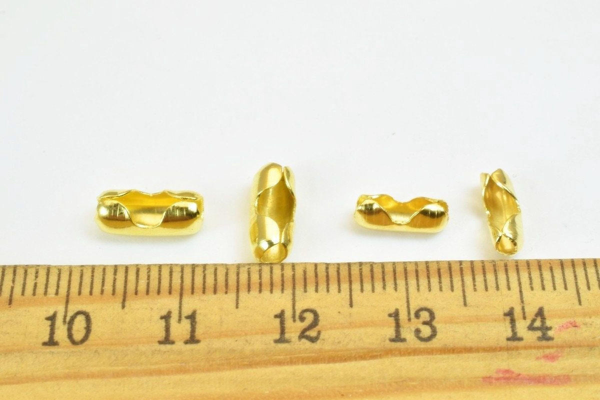 four gold-colored beads placed on a ruler for size comparison.