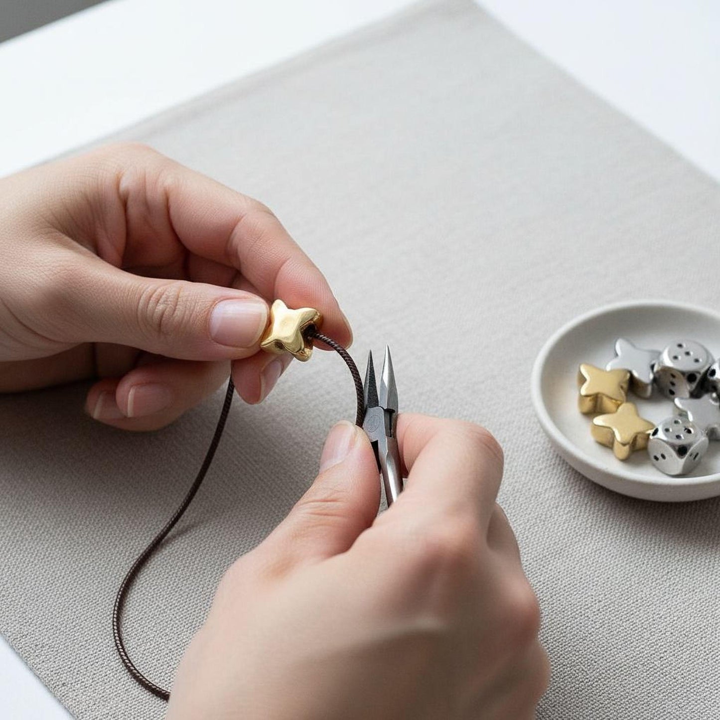 A person's hands are carefully crafting a necklace, using a pair of scissors to cut a star-shaped bead from a string.