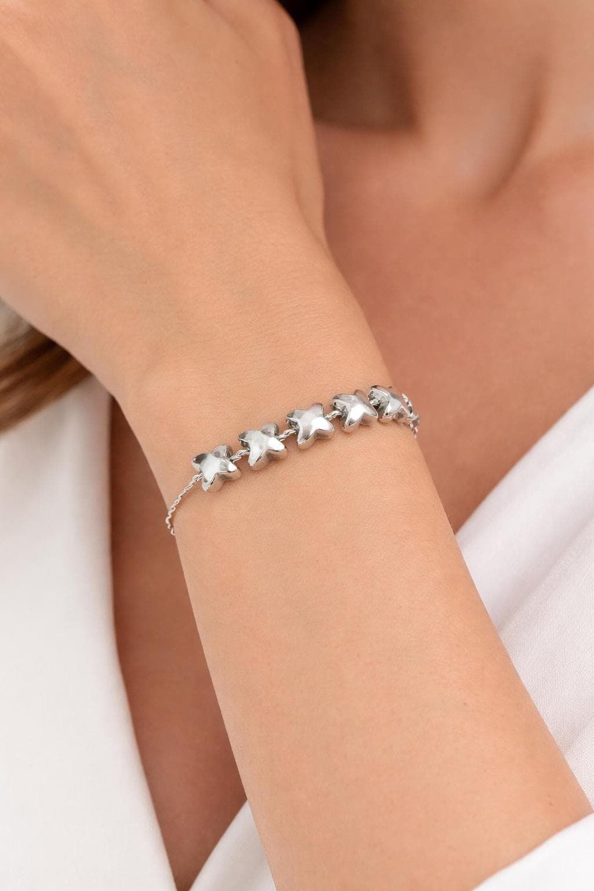 A close-up of a person's wrist wearing a silver bracelet with small star-shaped charms.
