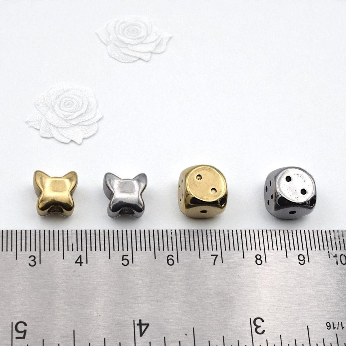 four different sizes of metal beads or charms, each placed next to a ruler for size comparison.