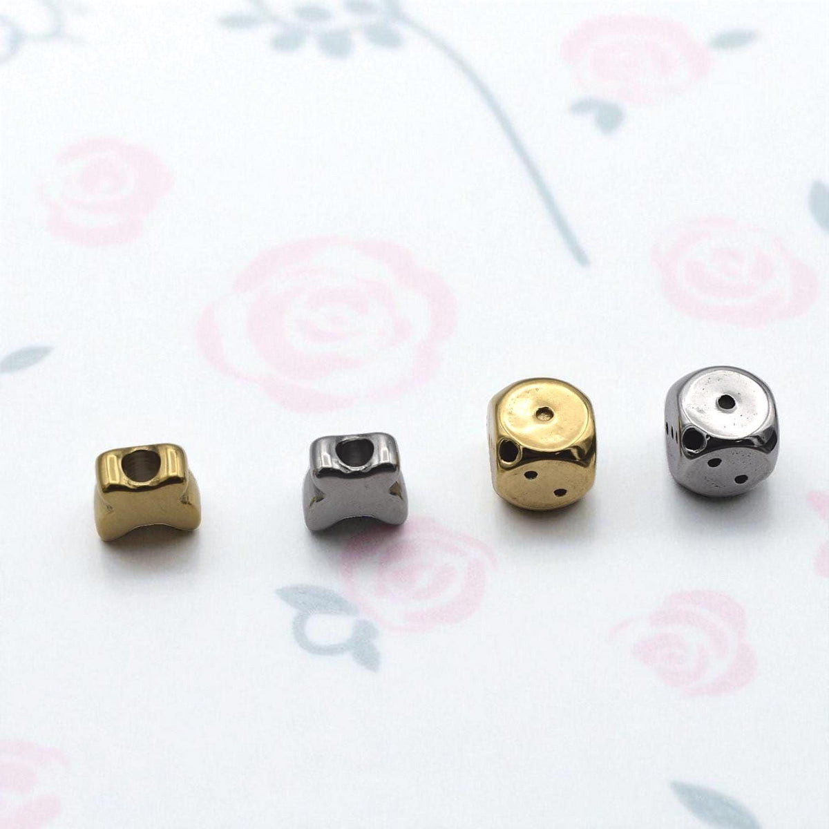 four different metal beads, each with a unique shape and size, arranged on a white background with a floral pattern.