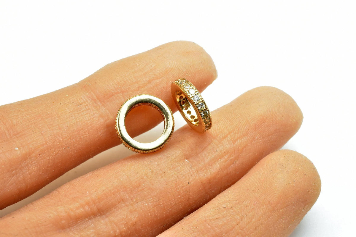 A close-up image of a person's hand holding two gold rings with small diamonds.