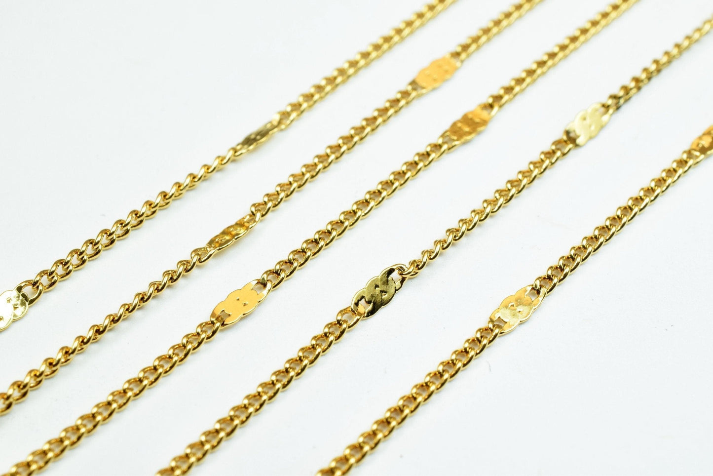A collection of gold-colored metal chain necklaces arranged diagonally on a white background.
