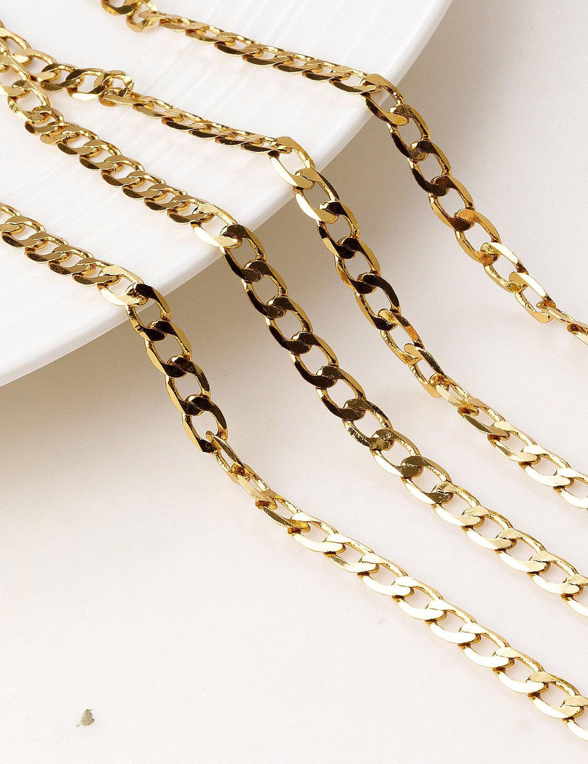 a close-up view of several gold-colored chain necklaces arranged on a white surface.